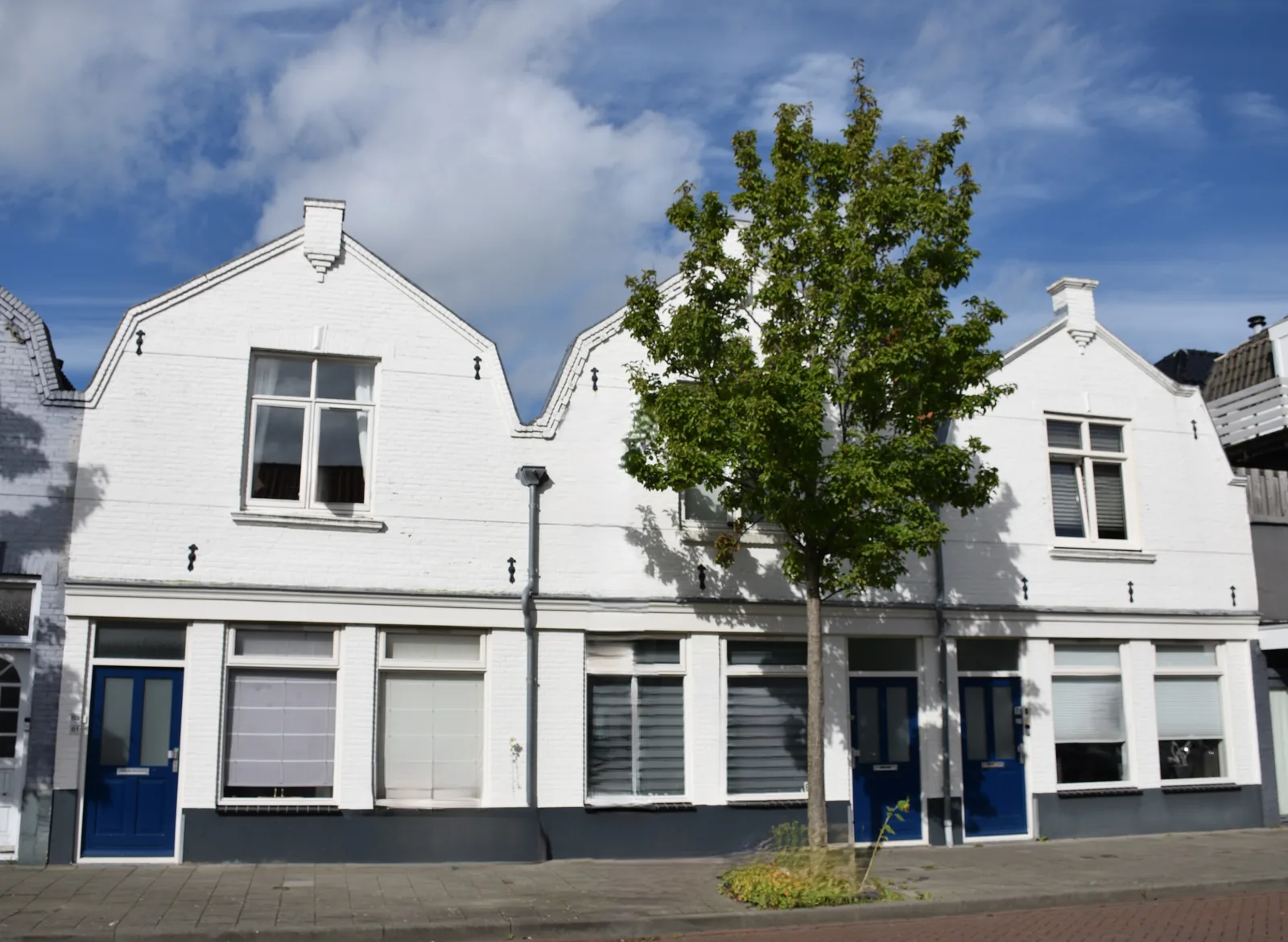 Witte jaren-dertig woningen aan een straat met een boom ervoor